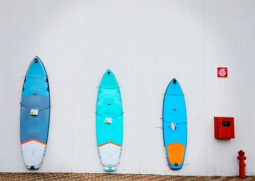 Free Three vibrant surfboards mounted on a white wall outdoors, with a brick base and safety box. Stock Photo