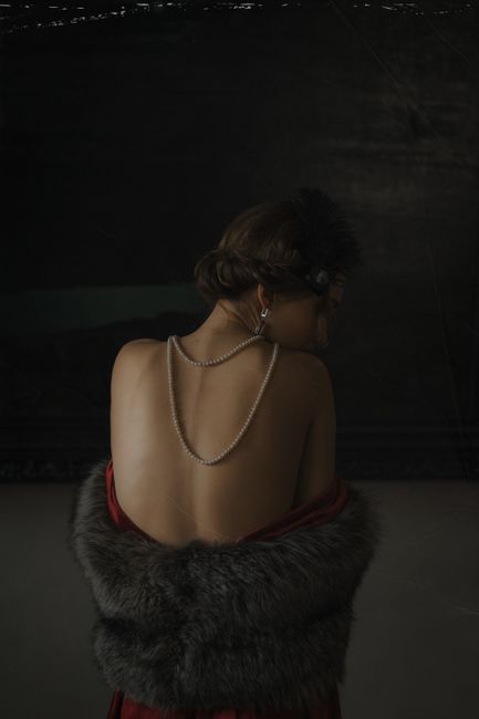 Elegant back view of a woman in vintage attire adorned with pearls and fur.