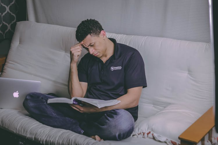 Man Sitting On Sofa Reading Book