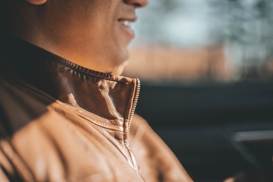 A man smiling in a brown leather jacket, bathed in warm daylight.