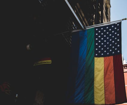 A striking image of a combined LGBTQ rainbow and American flag displayed outdoors during the day.