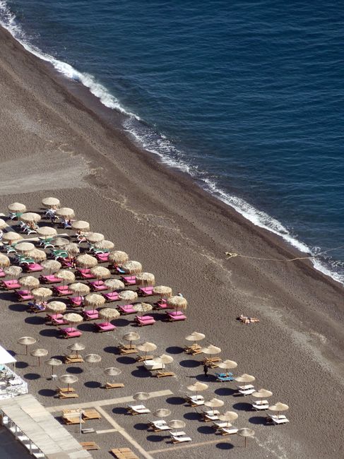 Aerial shot of Kamari Beach in Greece featuring umbrellas and sun beds on a sunny day.