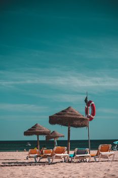 Relaxing tropical beach scene with loungers, umbrellas, and a calm sea under a clear sky.