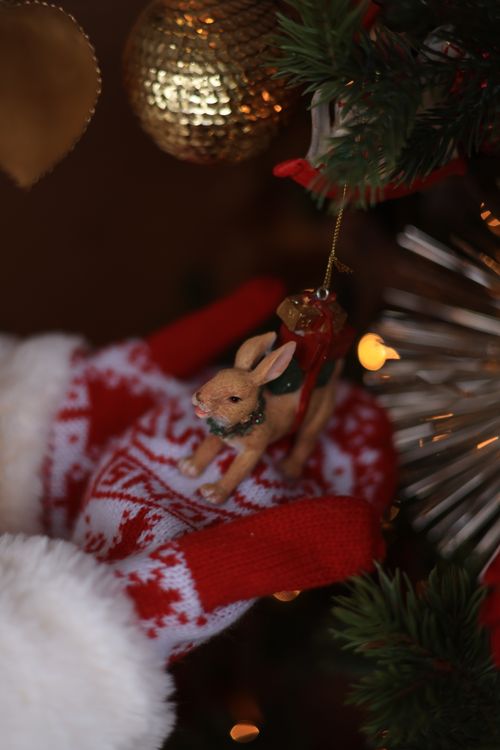 Free Close-up of a rabbit Christmas ornament held in gloves on a decorated tree. Stock Photo