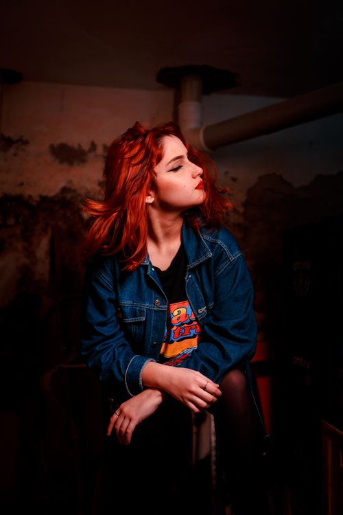 Free A redheaded woman in a denim jacket with closed eyes against a rustic backdrop. Stock Photo