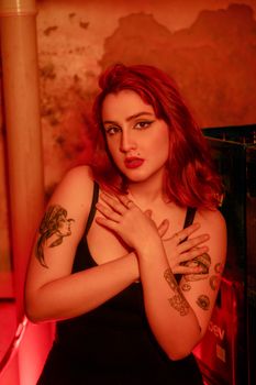 Striking portrait of tattooed woman with red hair in moody red lighting, showcasing fashion and self expression.