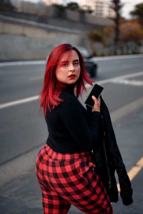 Free A fashionable red-haired woman holding a phone and jacket while walking on a city street. Stock Photo