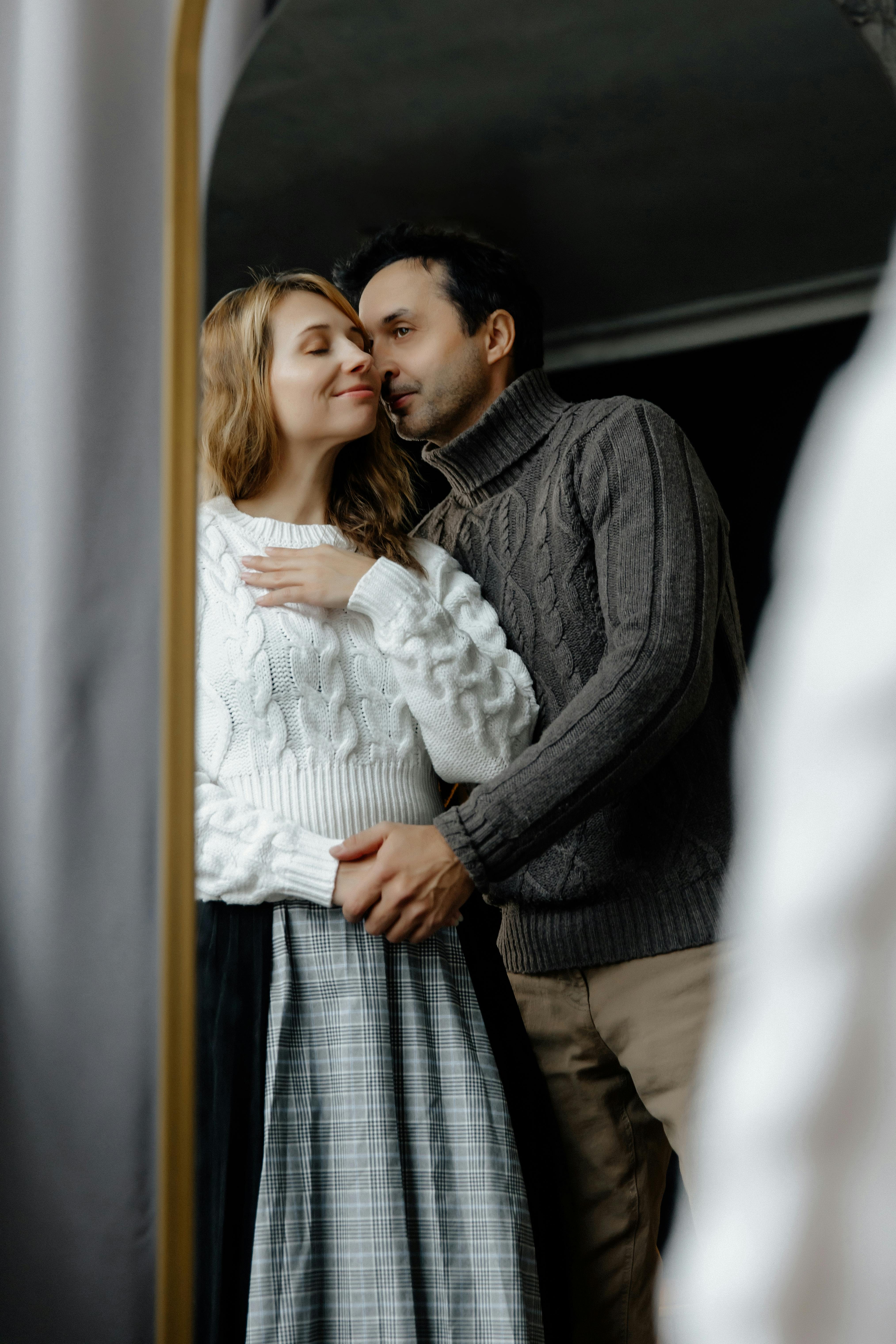 A loving couple embracing in warm sweaters, captured through a mirror reflection.