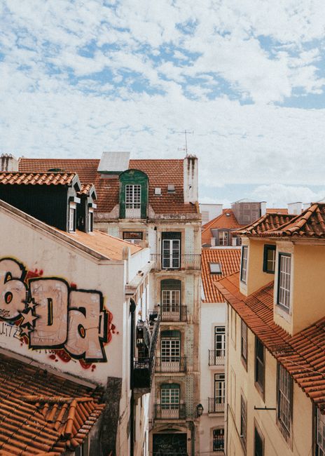 Colorful rooftops and traditional architecture in a Lisbon alleyway under a bright sky.