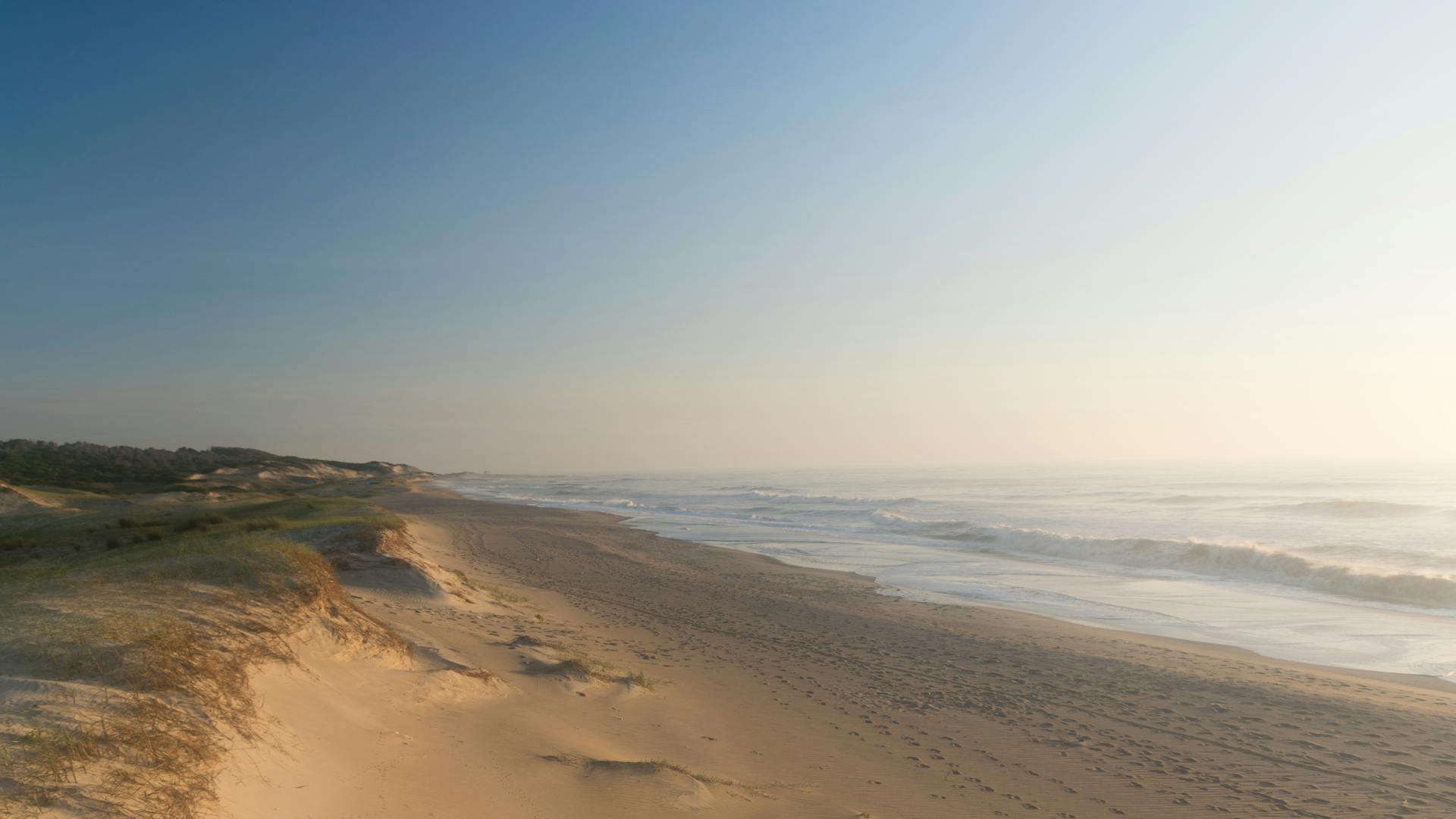 Peaceful sandy beach with ocean waves in Punta del Diablo, Uruguay during a sunny day.