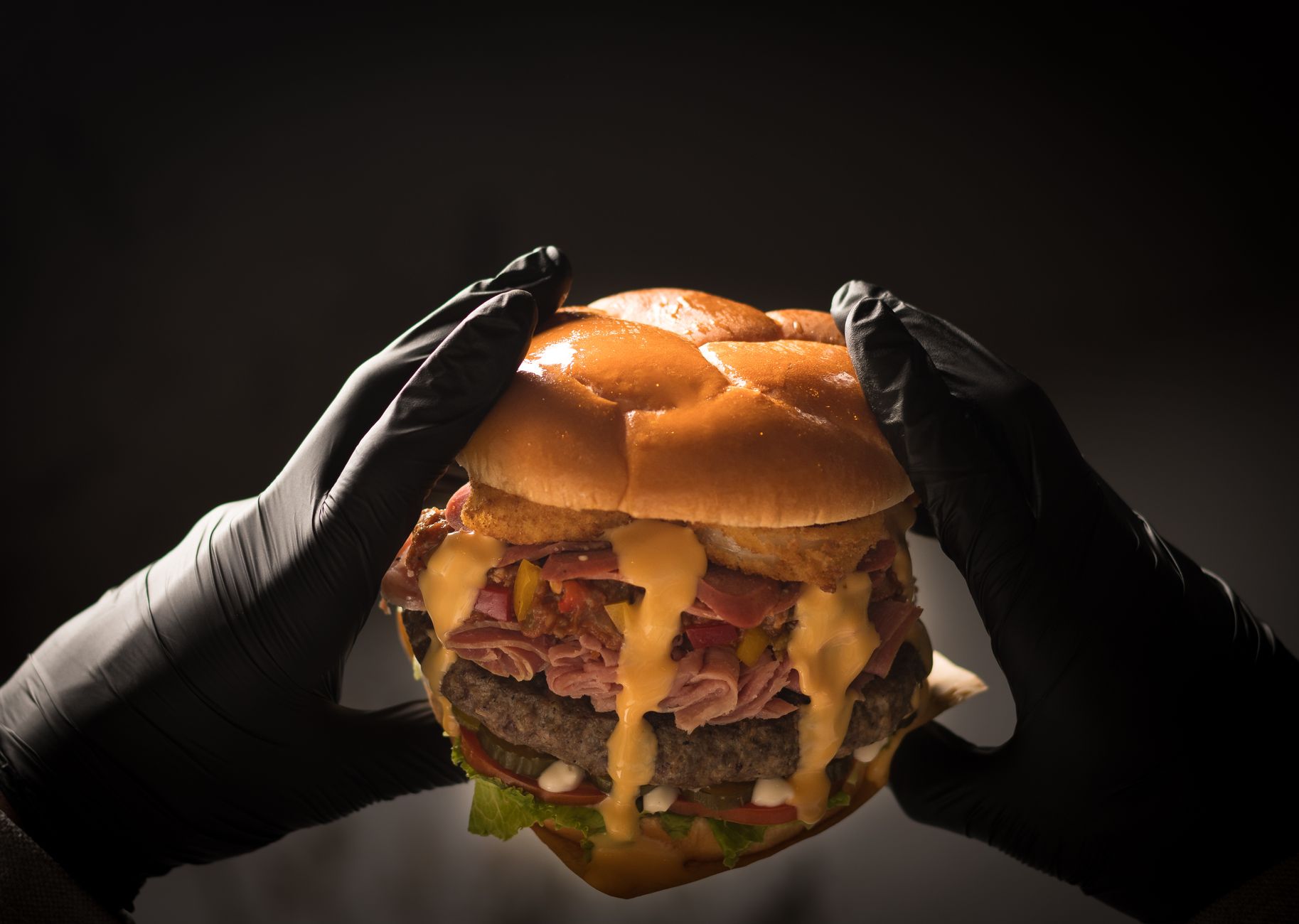 Close-up of a savory cheeseburger held by gloved hands against a black background.