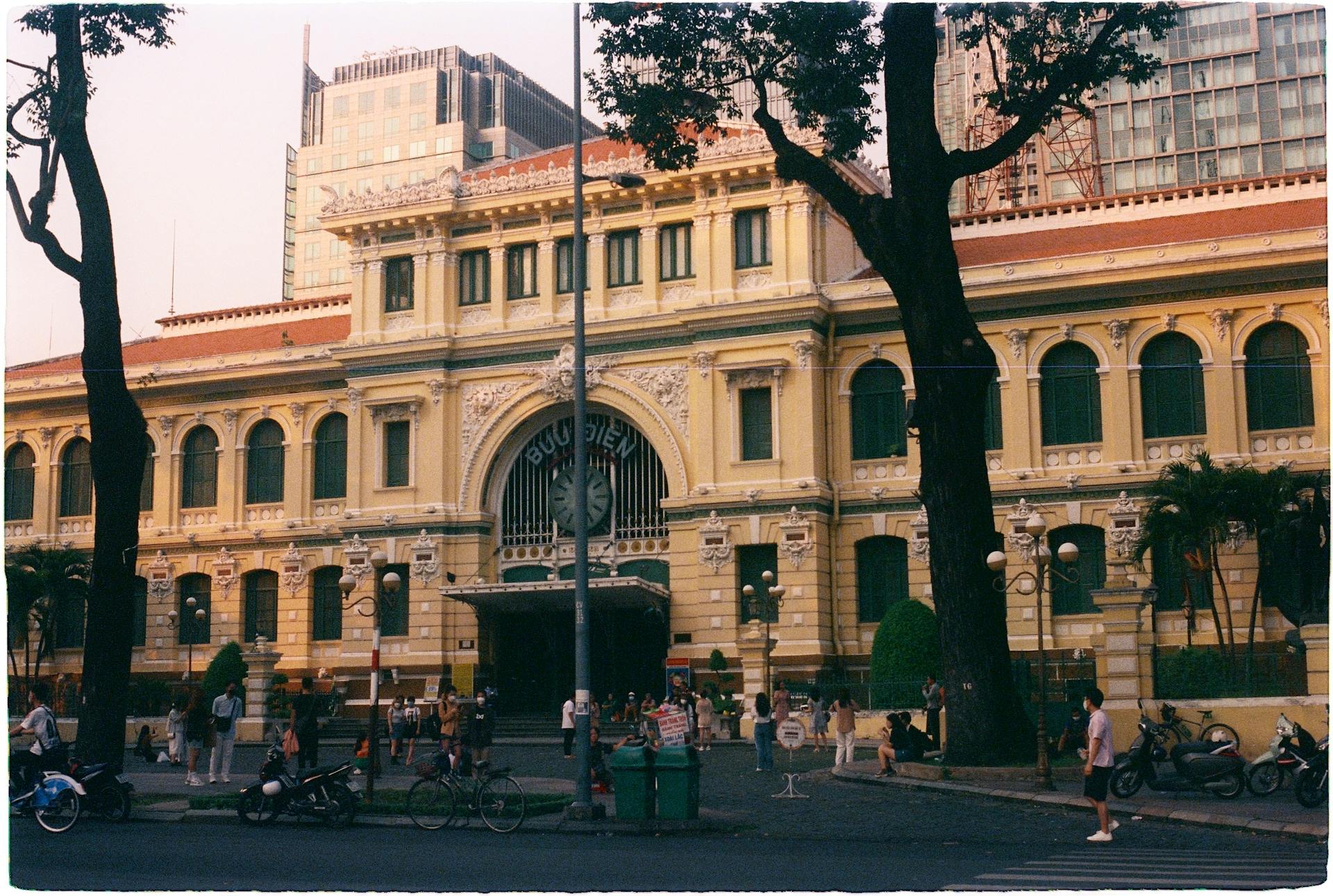 View of the iconic Saigon Central Post Office with people exploring its vicinity at dusk.