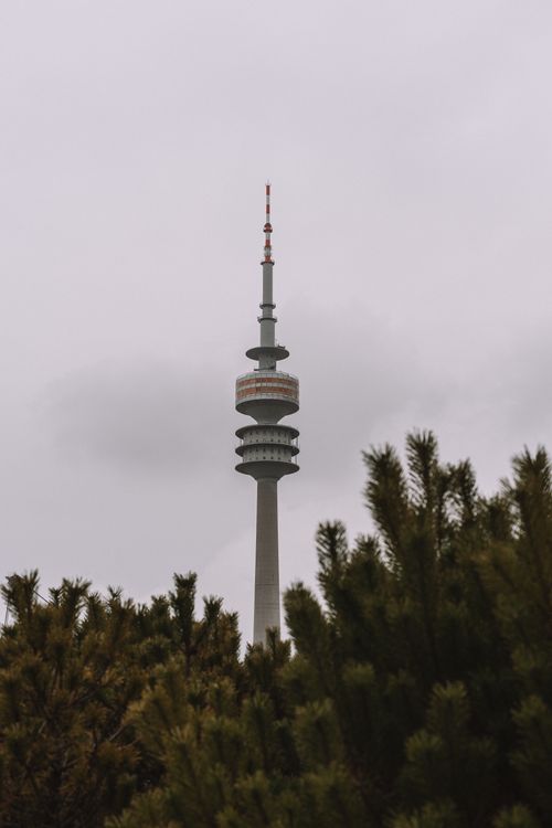 Free A tall broadcast tower surrounded by dark green trees against an overcast sky. Stock Photo