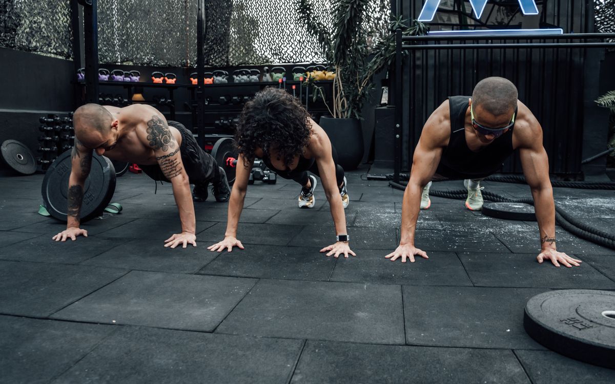 Three individuals performing push-ups together in a Mexico City gym setting.
