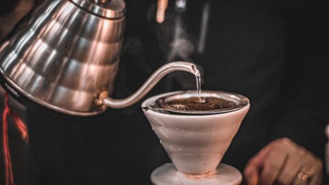 Steam rises as hot water is poured over coffee grounds in a pour-over coffee maker.