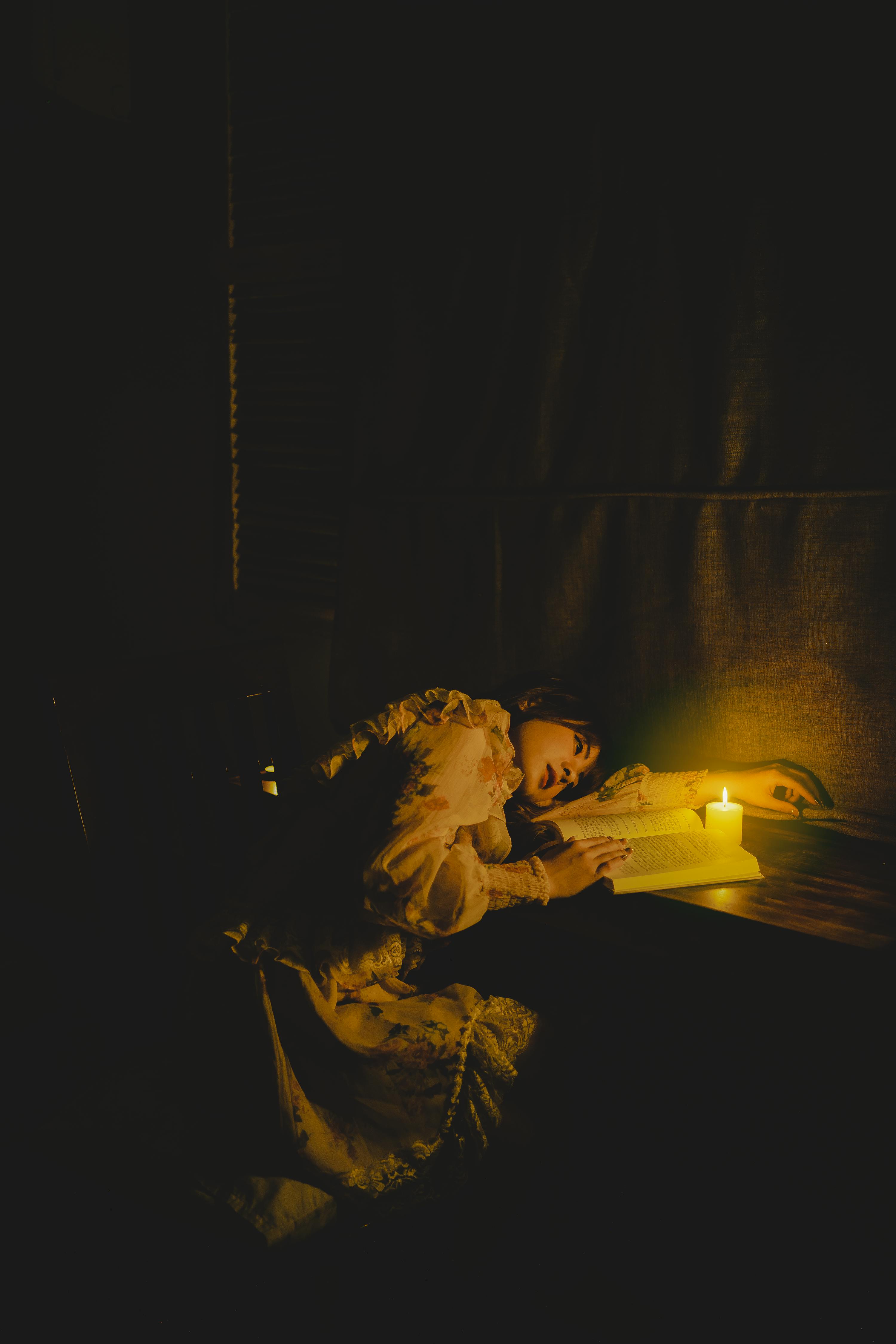 woman lying down on table and reading book with wax candle