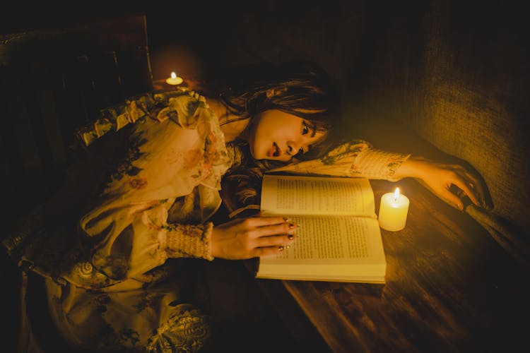 Woman Reading Book With Wax Candle On Table