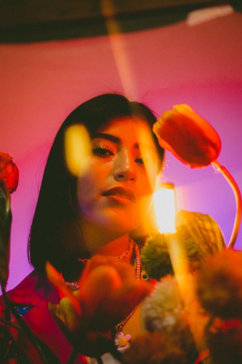 Free Artistic portrait of a woman surrounded by colorful flowers and warm light. Stock Photo
