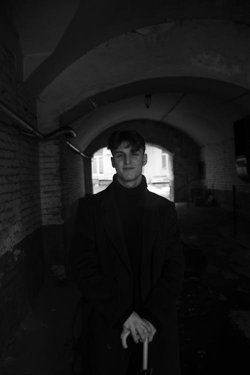 Grayscale Photo of a Man Wearing Black Coat inside the Tunnel