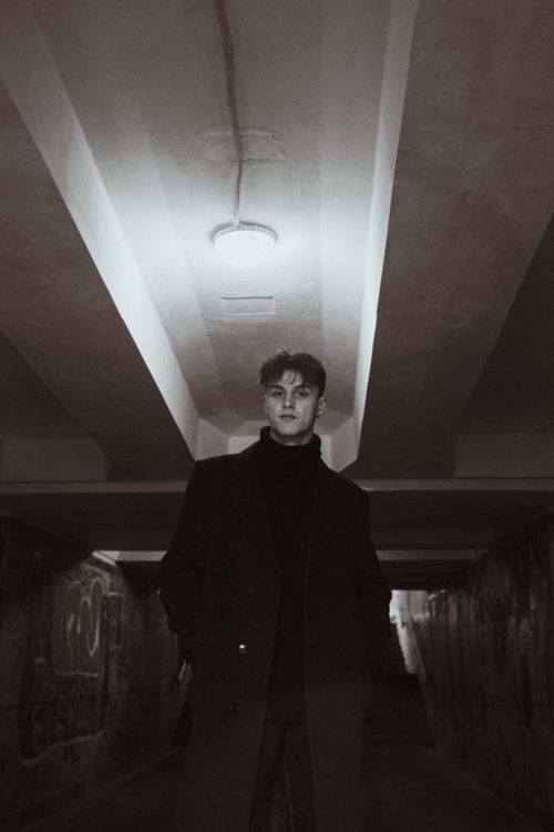 Free A man in a black coat poses in a graffiti-covered urban underground, featuring a dramatic low-angle shot. Stock Photo