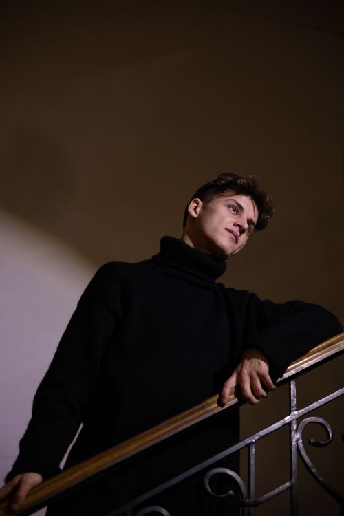 Free Portrait of a man in a black sweater leaning on a staircase indoors. Stock Photo