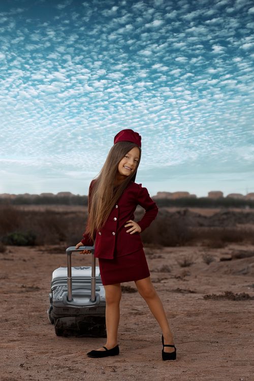 Free Charming young girl dressed as a flight attendant with luggage in a desert landscape. Stock Photo