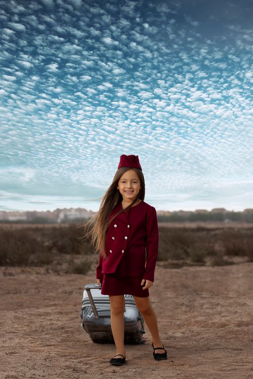 Free Adorable young girl dressed in a stylish uniform posing outdoors with a suitcase. Perfect for travel and fashion themes. Stock Photo