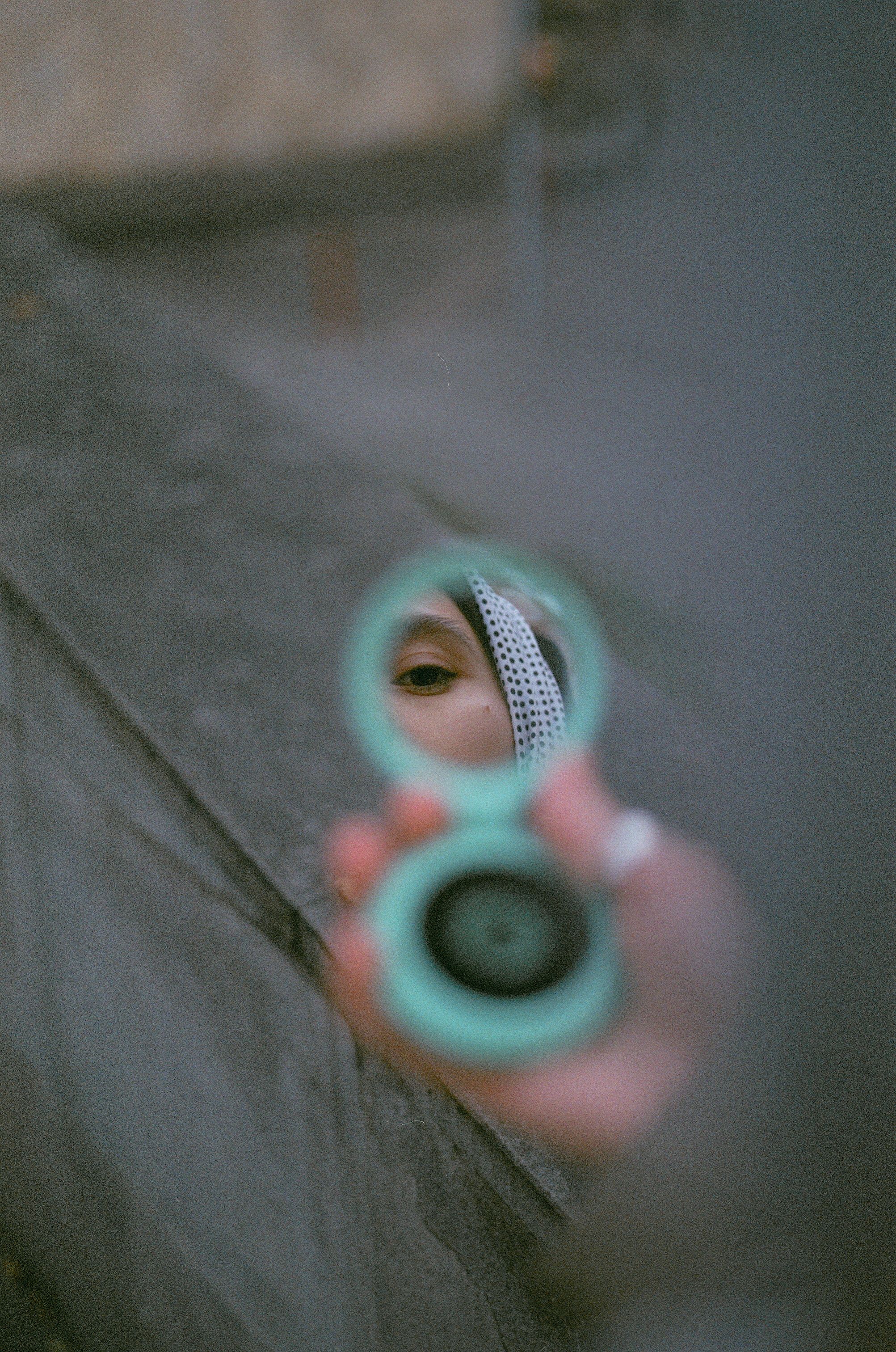 A woman wearing a headscarf is reflected in a hand mirror in an outdoor setting in Yerevan, Armenia.