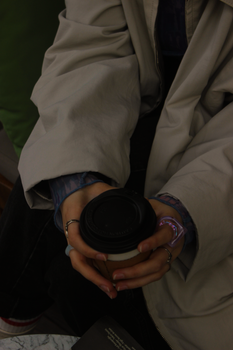 Close-up of hands in a jacket holding a disposable coffee cup indoors.