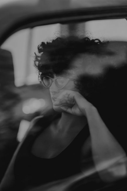 Black and white photo of a woman with curly hair seated in a car, looking contemplative.