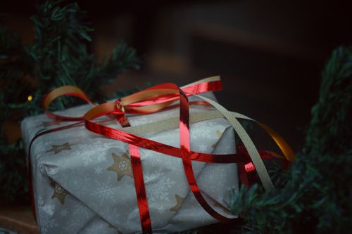 Free Close-up of a wrapped gift with red ribbon under a Christmas tree branch. Stock Photo