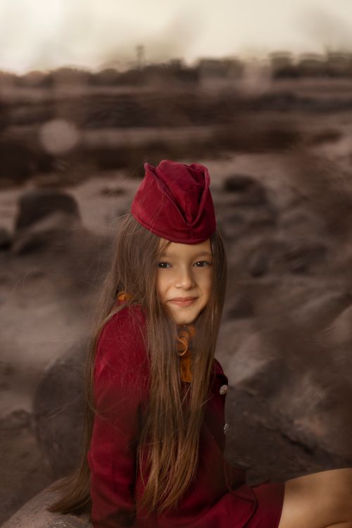 Free A young girl wearing a vintage outfit sits on rocky terrain, evoking a classic and timeless feel. Stock Photo