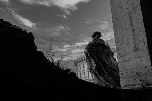 Grayscale Photo of a Statue Beside the Concrete Wall 