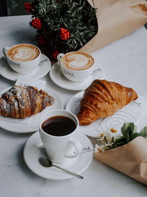 Free Elegant French breakfast setting with coffee, cappuccino, croissants, and flowers on marble table. Stock Photo