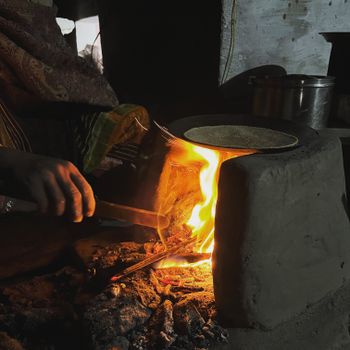 Close-up of traditional cooking on a clay stove with open fire and hands.
