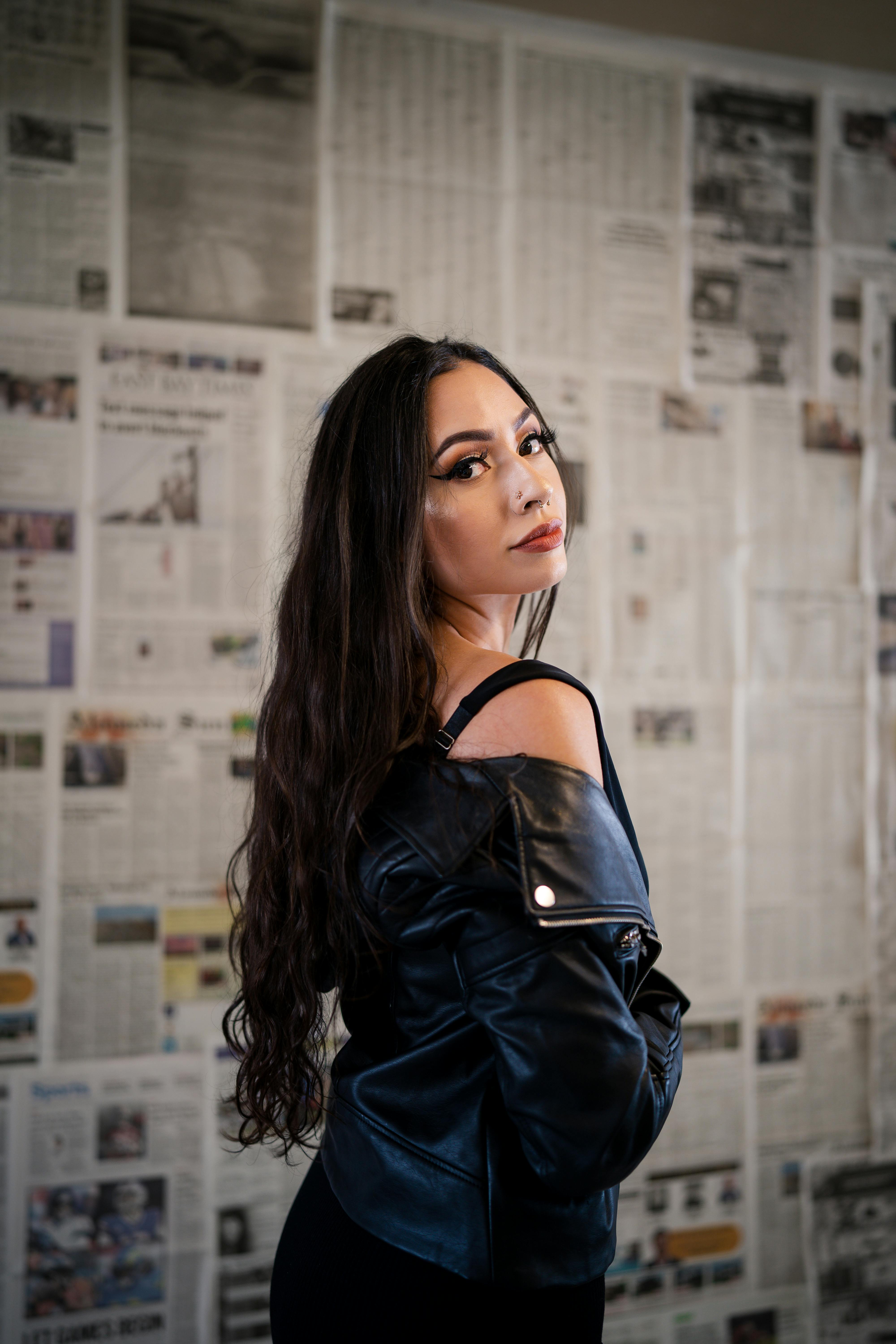 Elegant woman in leather jacket posing against a newspaper-covered wall.
