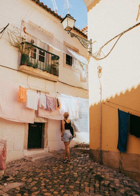 Woman walking in a sunny Lisbon alley with hanging laundry and cobblestone path.