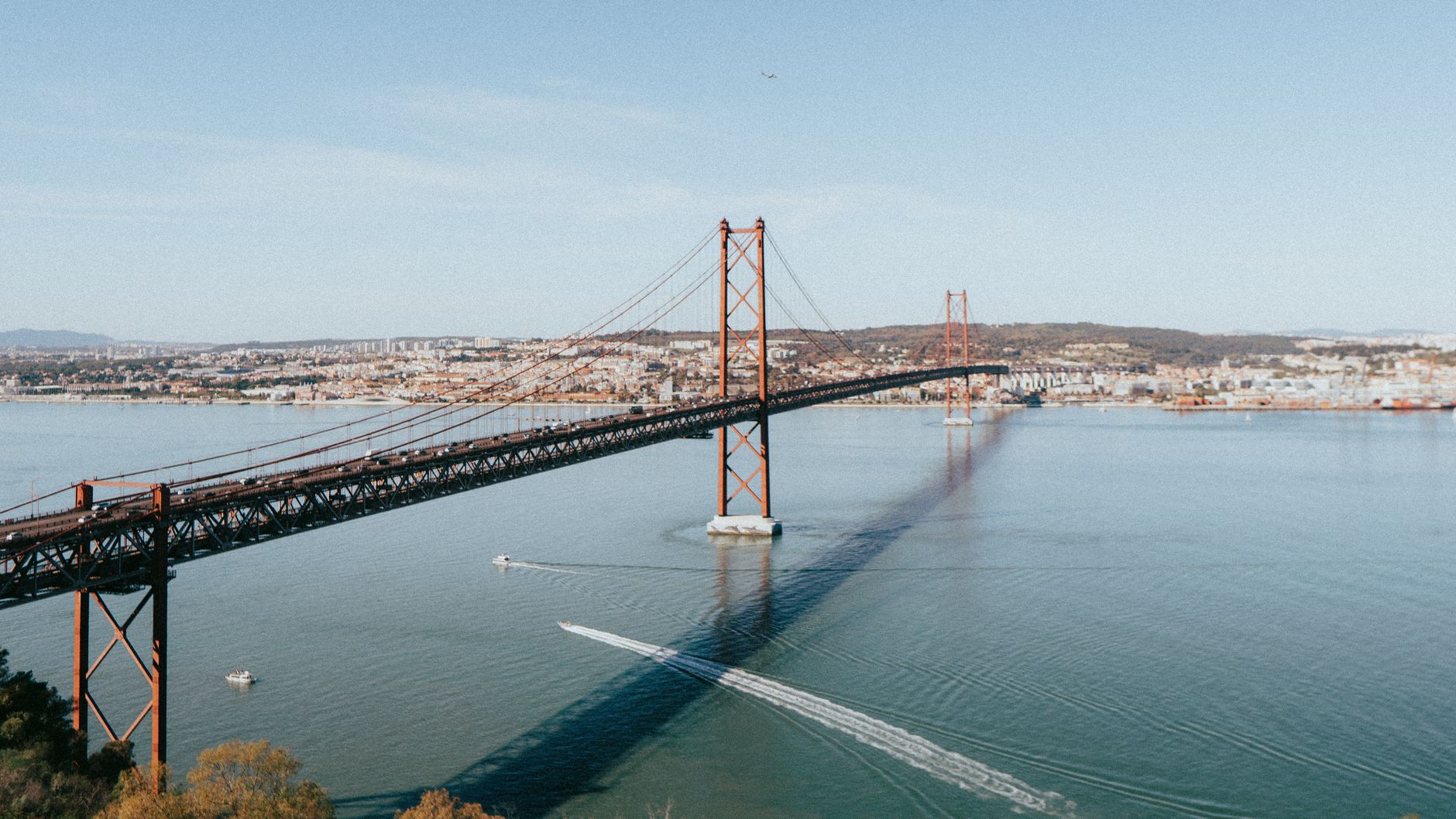 A stunning view of the 25 de Abril Bridge spanning the Tagus River in Lisbon, Portugal, on a sunny day.
