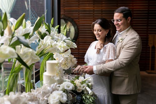 Newlyweds Smiling by Table with Wedding Cake and Flowers