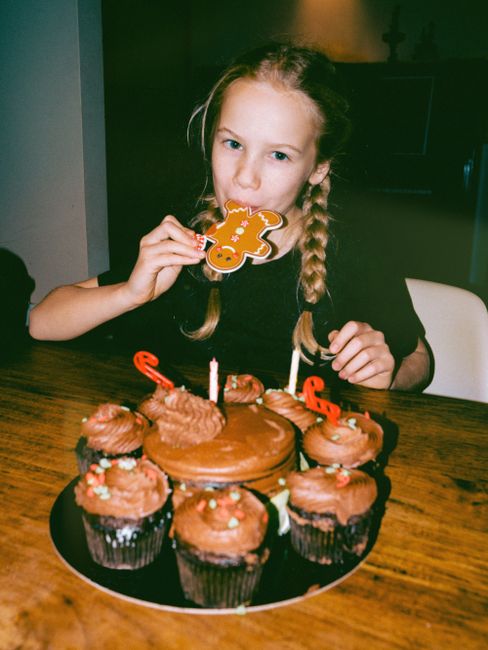 Young girl bites into a gingerbread cookie surrounded by chocolate cupcakes, creating a festive atmosphere.