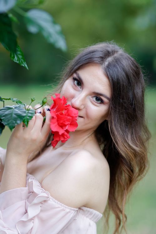 Free A woman enjoying the fragrance of a bright red flower in a natural outdoor setting. Stock Photo