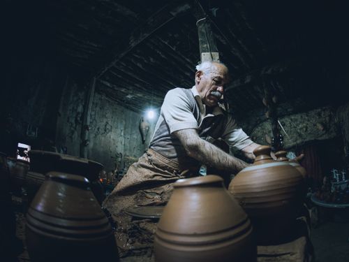 Free A focused elderly artisan works on pottery vases inside a dimly-lit workshop. Stock Photo