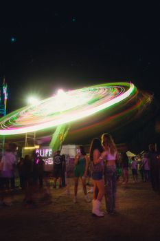 Dynamic nighttime scene of a spinning carnival ride with colorful neon lights and people enjoying the festival atmosphere.