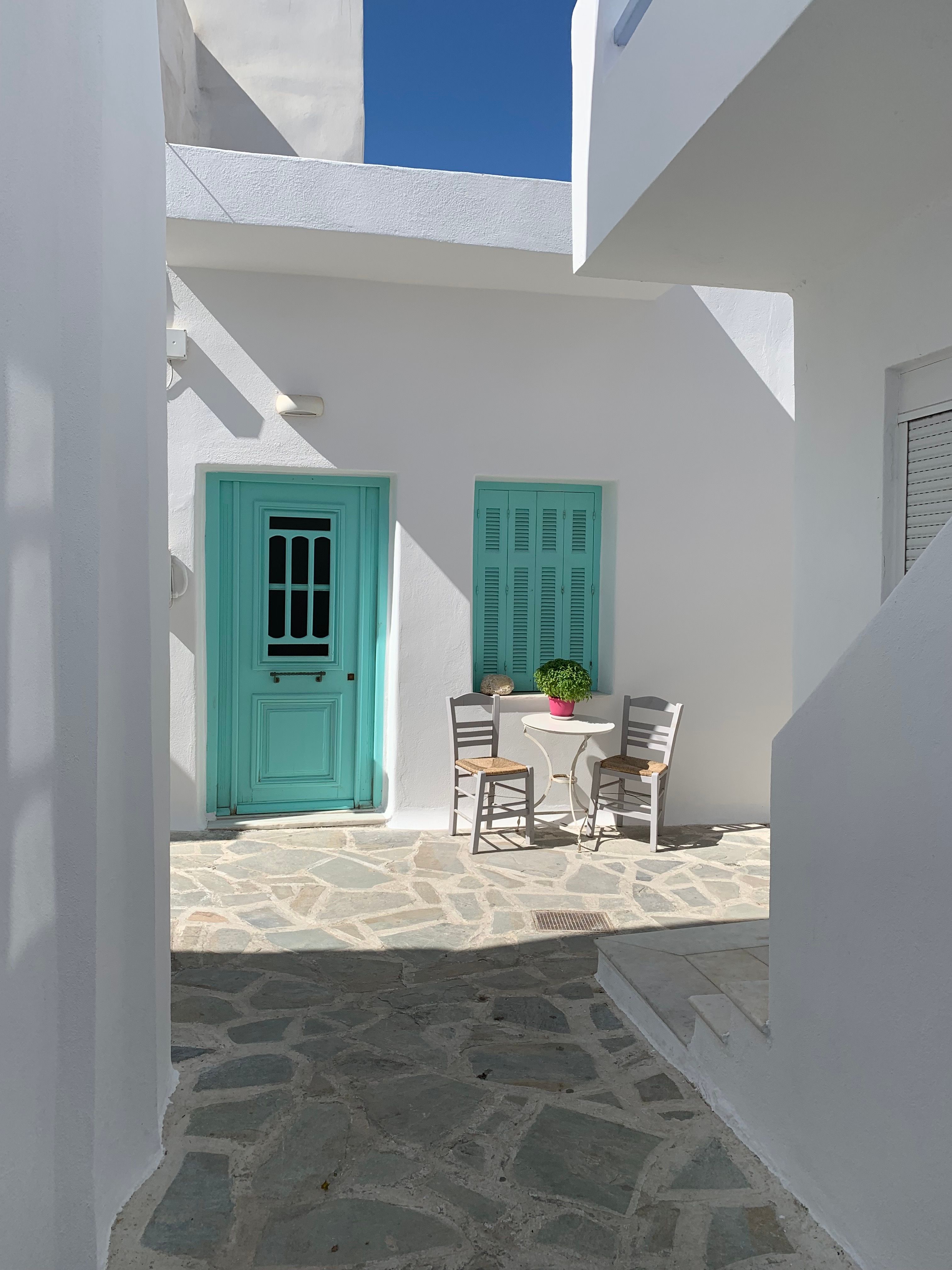 Sunlit courtyard in Naxos, Greece featuring a turquoise door and traditional architecture.