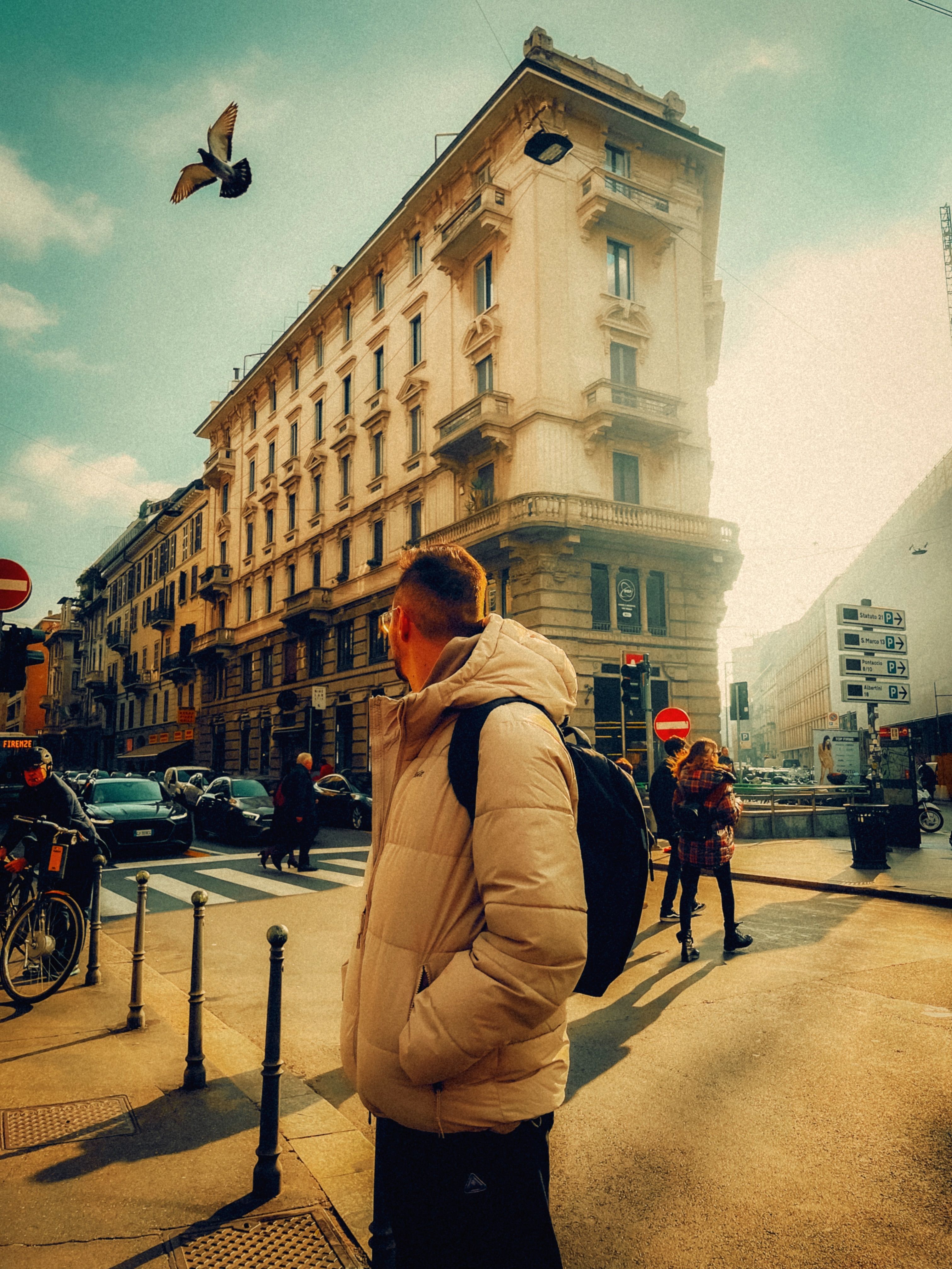 Urban street scene in Milan, featuring a historic building, people, and a pigeon flying over.