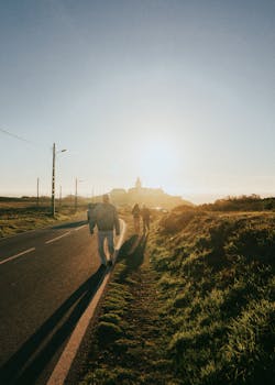 People walking beside a road at sunrise in a scenic countryside setting.