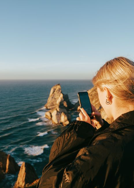Woman captures breathtaking ocean view from Portuguese cliffs on a sunny day.