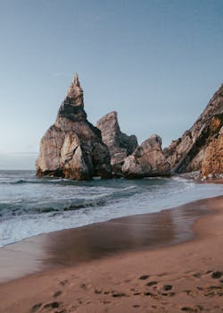 Stunning scenic view of rugged cliffs and waves at Praia da Ursa in Portugal during a warm sunset.