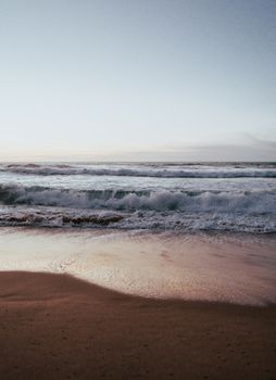 Calm ocean waves crashing at dawn on a sandy beach, creating a tranquil atmosphere.