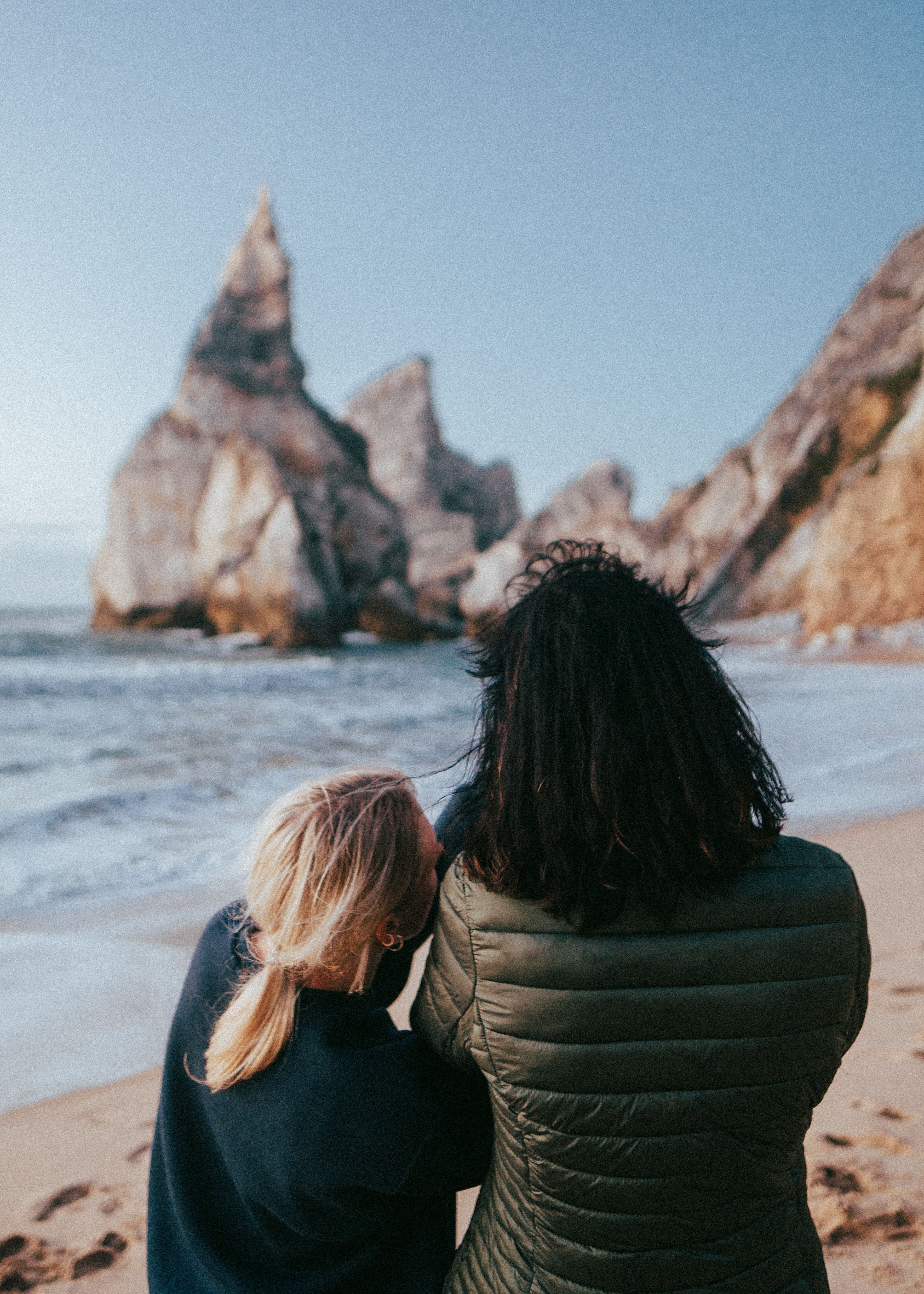 Two people embracing while enjoying a scenic view of the beach with majestic rock formations.